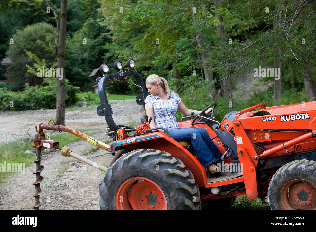 Jeune Femme Blonde Au Volant Du Tracteur Kubota Avec Bêche Tarière à La Ferme De Travail 